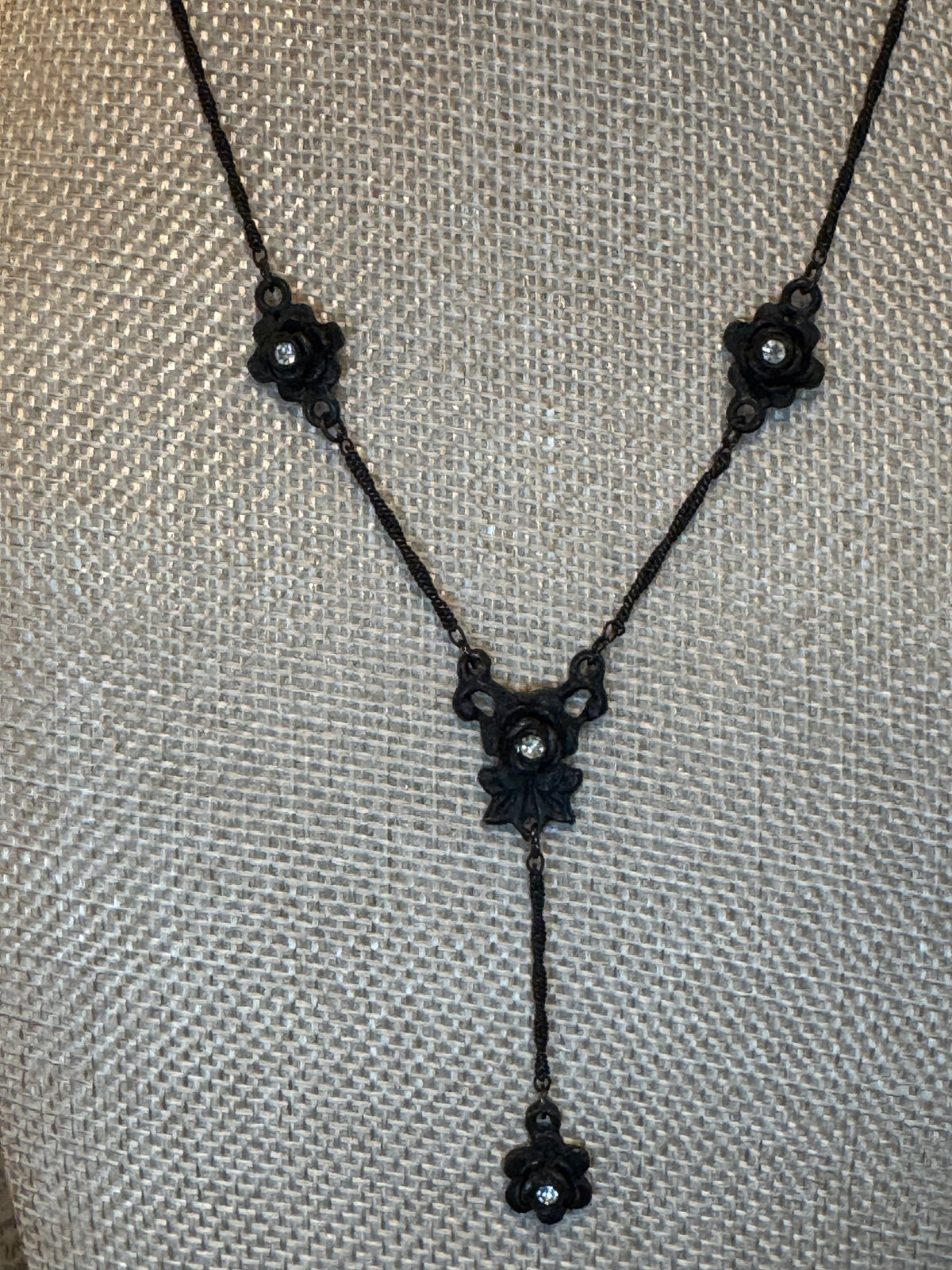 Antiqued black metal necklace featuring floral-shaped stations accented with small clear rhinestones