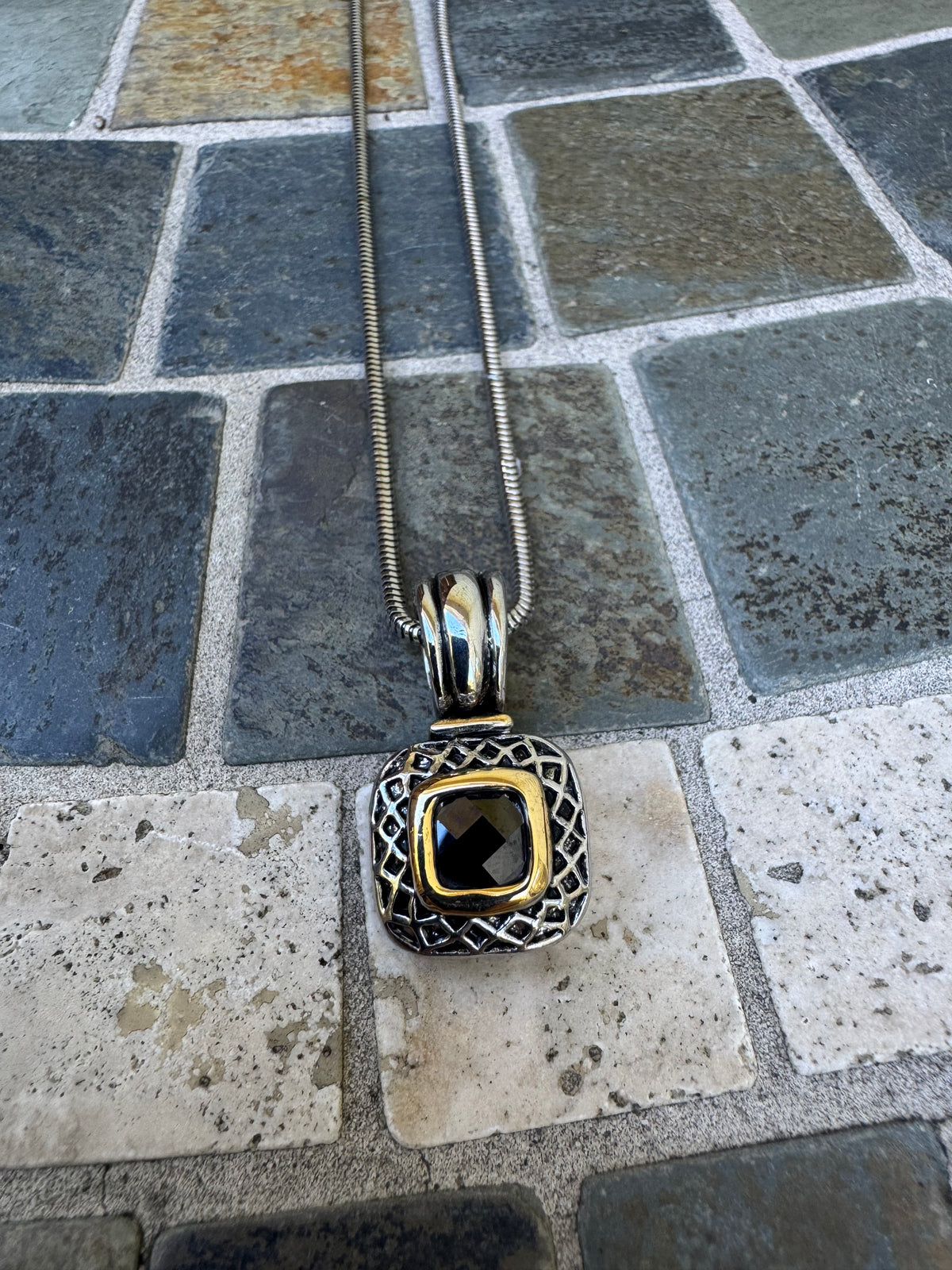 Pendant Necklace Featuring a Black Gemstone Set in a Textured Silver and Gold-accented Frame