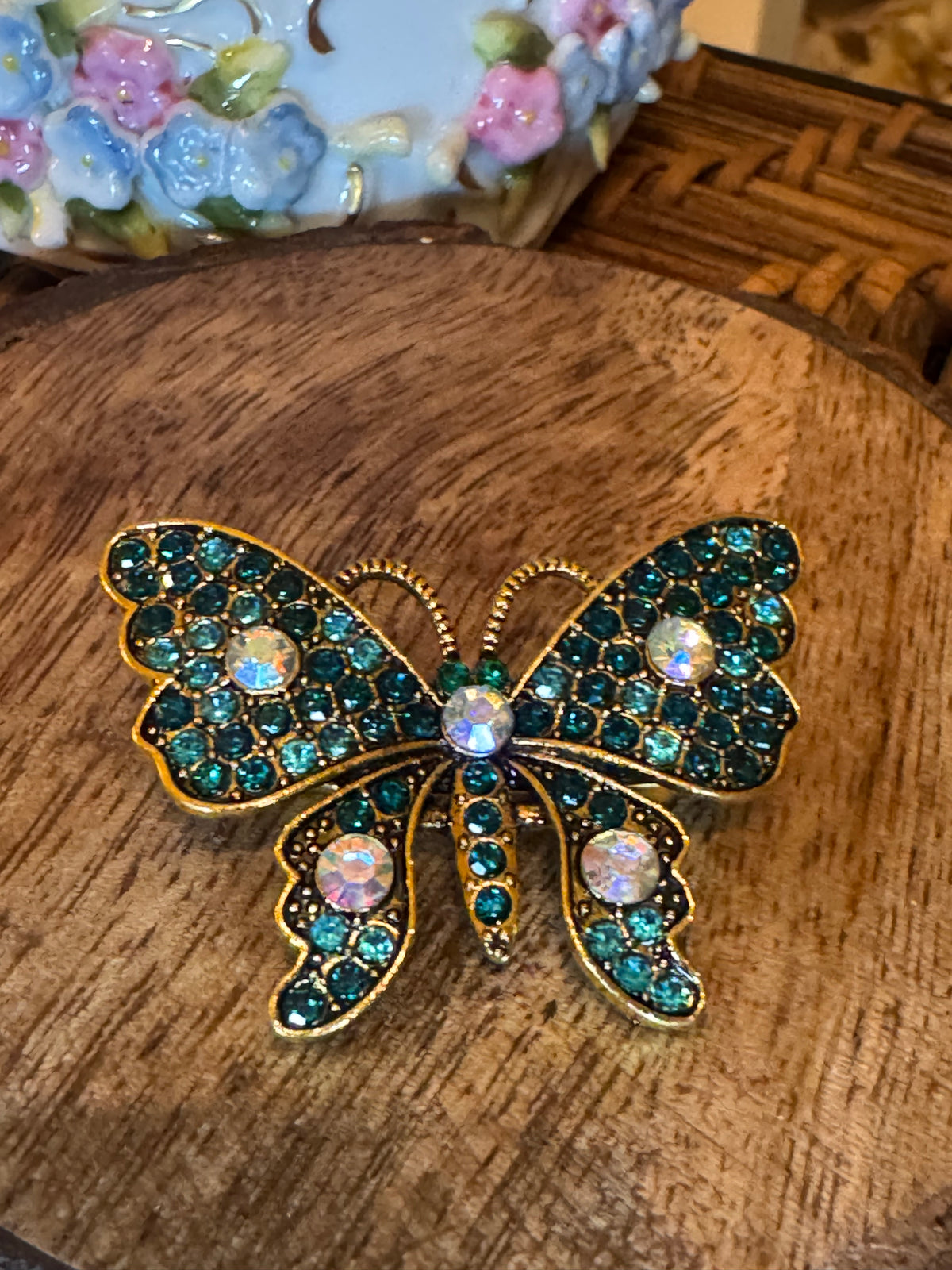 Gold-tone butterfly brooch features sparkling teal and iridescent rhinestone crystals