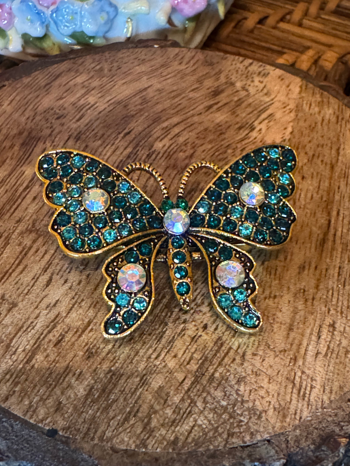 Gold-tone butterfly brooch features sparkling teal and iridescent rhinestone crystals