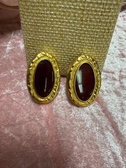 Vintage, gold-tone button earrings featuring a textured rope-style border surrounding a dark red, oval cabochon stone