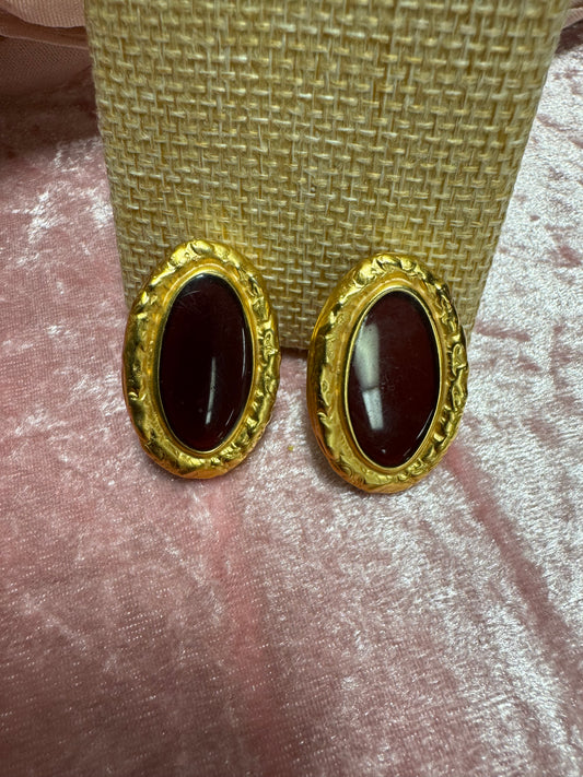 Vintage, gold-tone button earrings featuring a textured rope-style border surrounding a dark red, oval cabochon stone