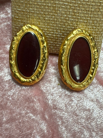 Vintage, gold-tone button earrings featuring a textured rope-style border surrounding a dark red, oval cabochon stone