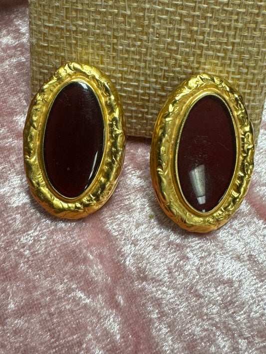 Vintage, gold-tone button earrings featuring a textured rope-style border surrounding a dark red, oval cabochon stone