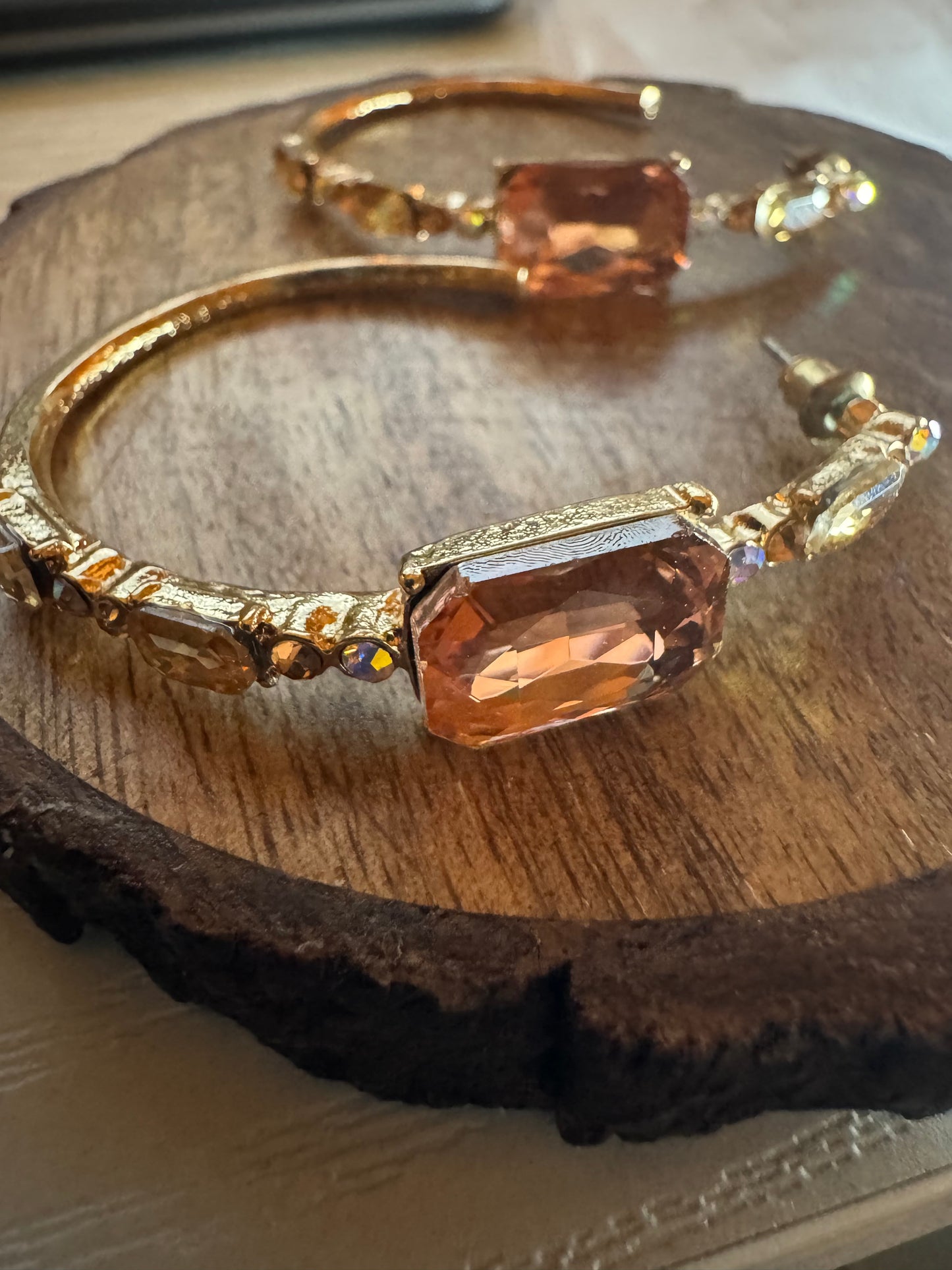 Gold tone hoop earrings featuring large peach-colored rhinestones