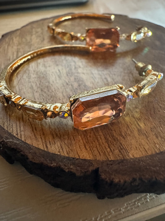 Gold tone hoop earrings featuring large peach-colored rhinestones