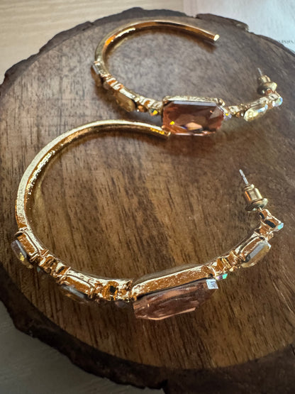 Gold tone hoop earrings featuring large peach-colored rhinestones