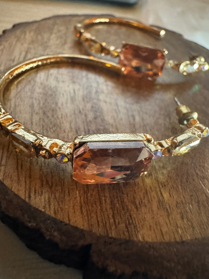 Gold tone hoop earrings featuring large peach-colored rhinestones